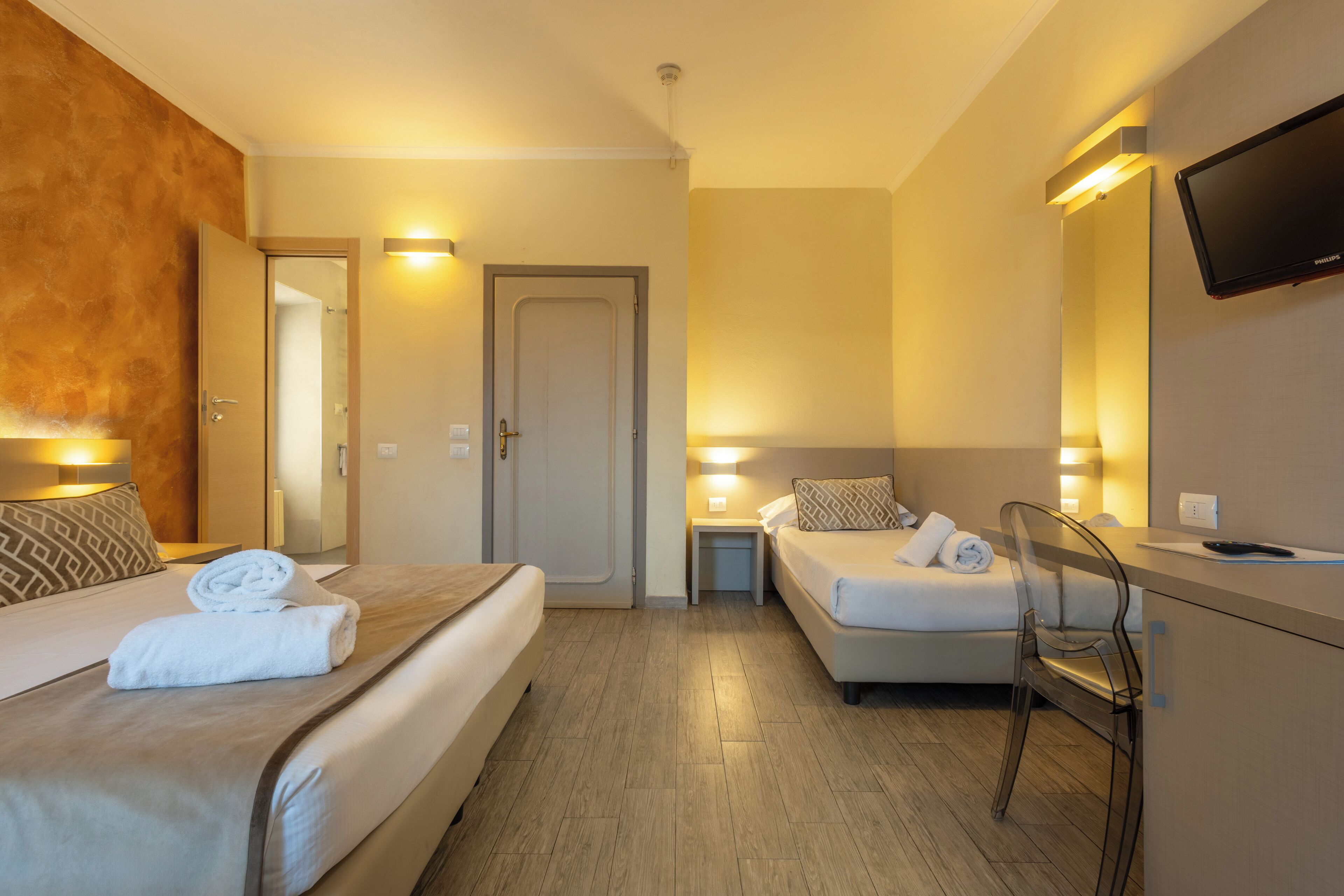 A hotel room with two beds, a desk, a chair, and a TV.