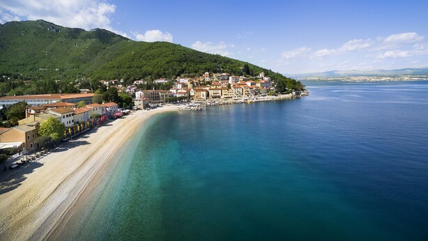 Un pueblo costero con playa, edificios y montañas al fondo.