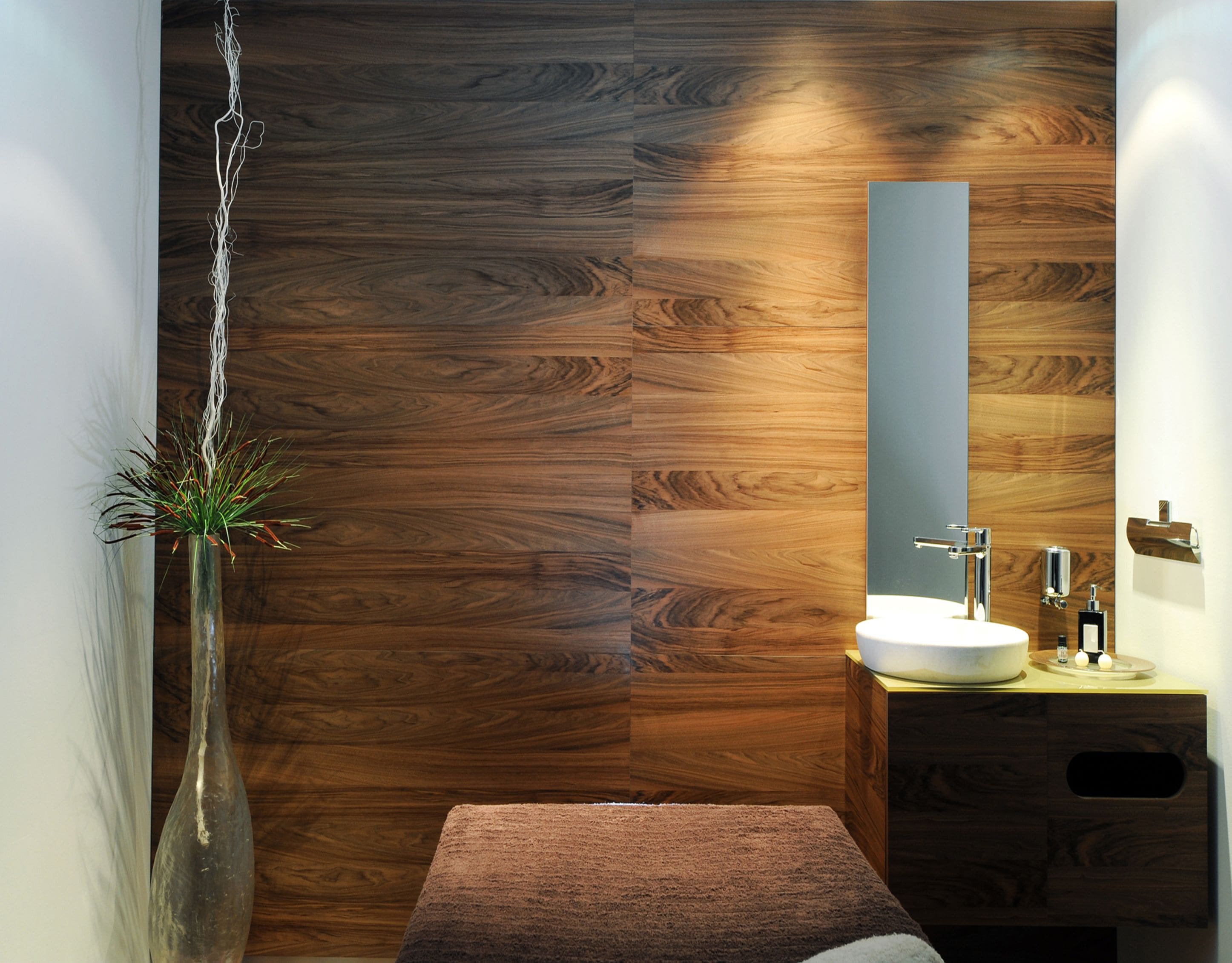 Un baño moderno con pared de madera, un lavabo blanco, un espejo y una planta en un florero.