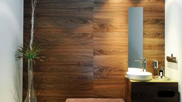 Un baño moderno con pared de madera, un lavabo blanco, un espejo y una planta en un florero.