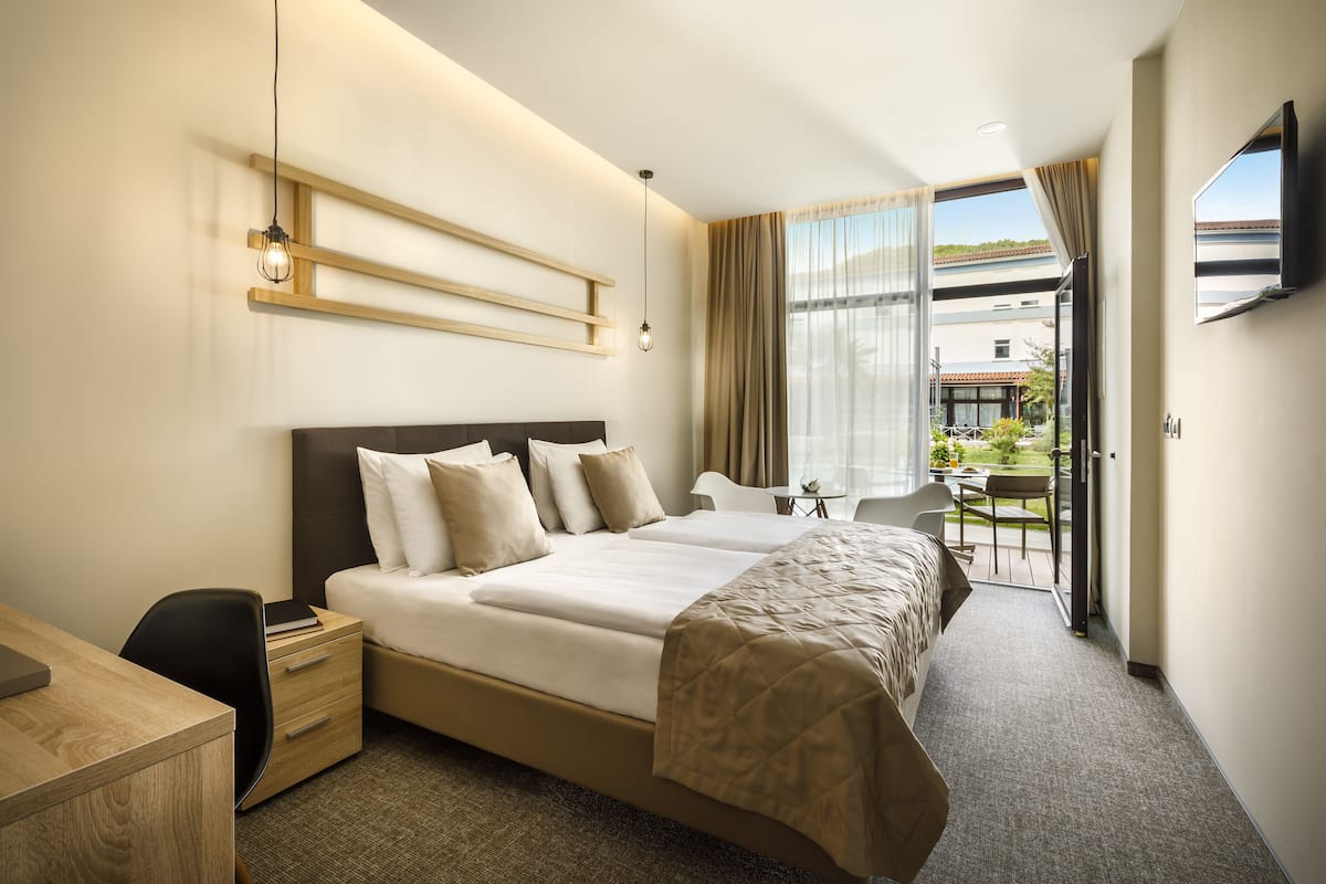 A hotel room with a large bed, a desk, and a balcony with a table and chairs.
