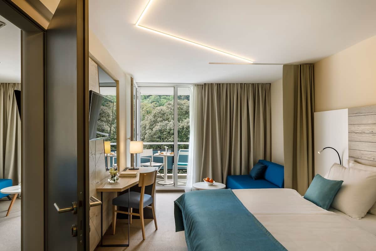 A hotel room with a bed, a desk with a chair, a small table, and a view of the outdoors.