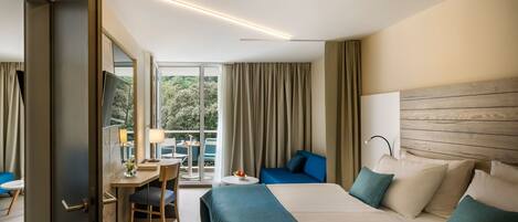 A hotel room with a bed, a desk with a chair, a small table, and a view of the outdoors.