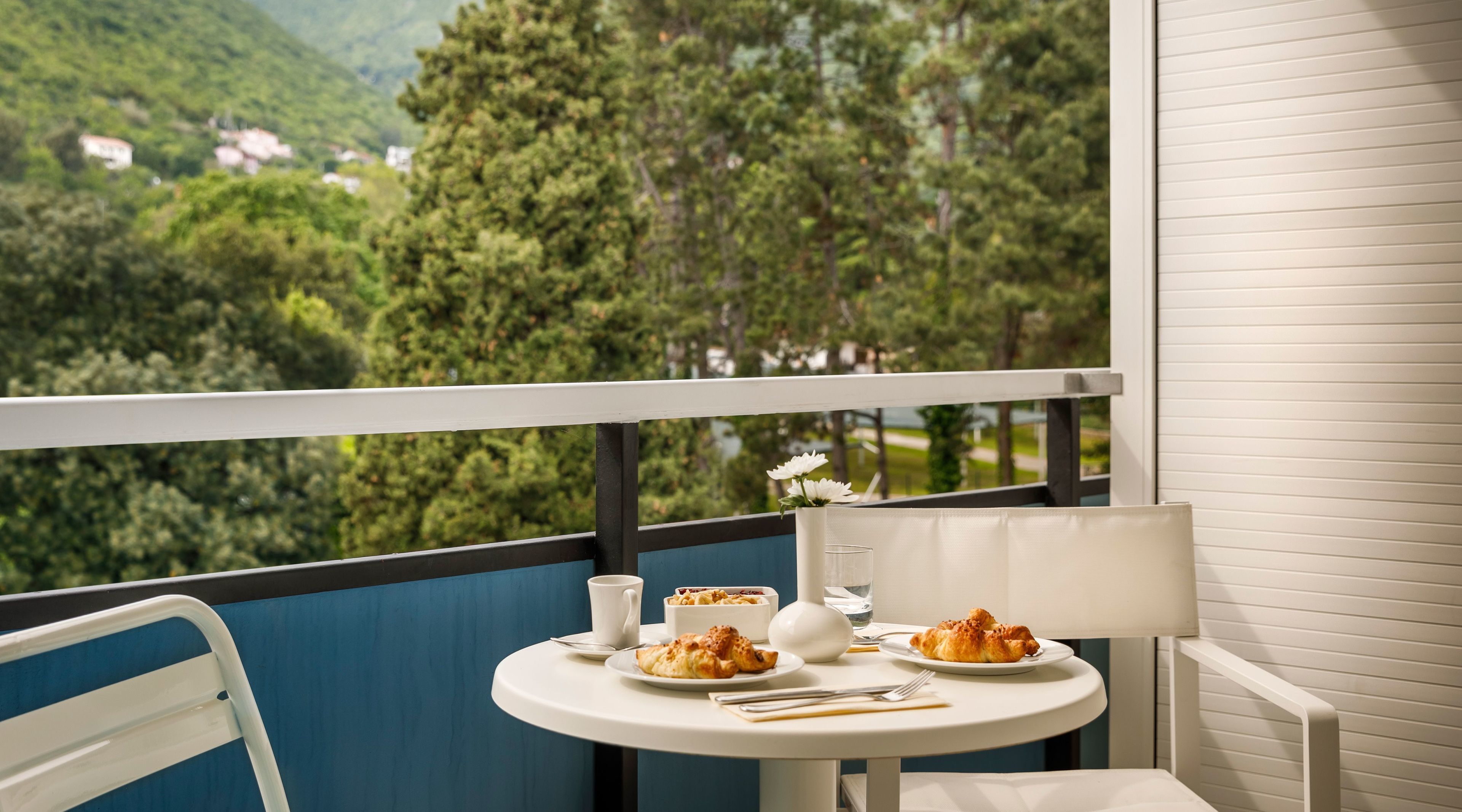 A balcony with a table set for two, overlooking a lush green landscape.