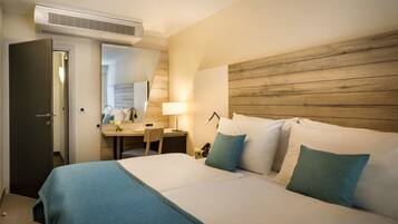 Quarto de hotel com cama, mesa de cabeceira, abajur e cabeceira de madeira.