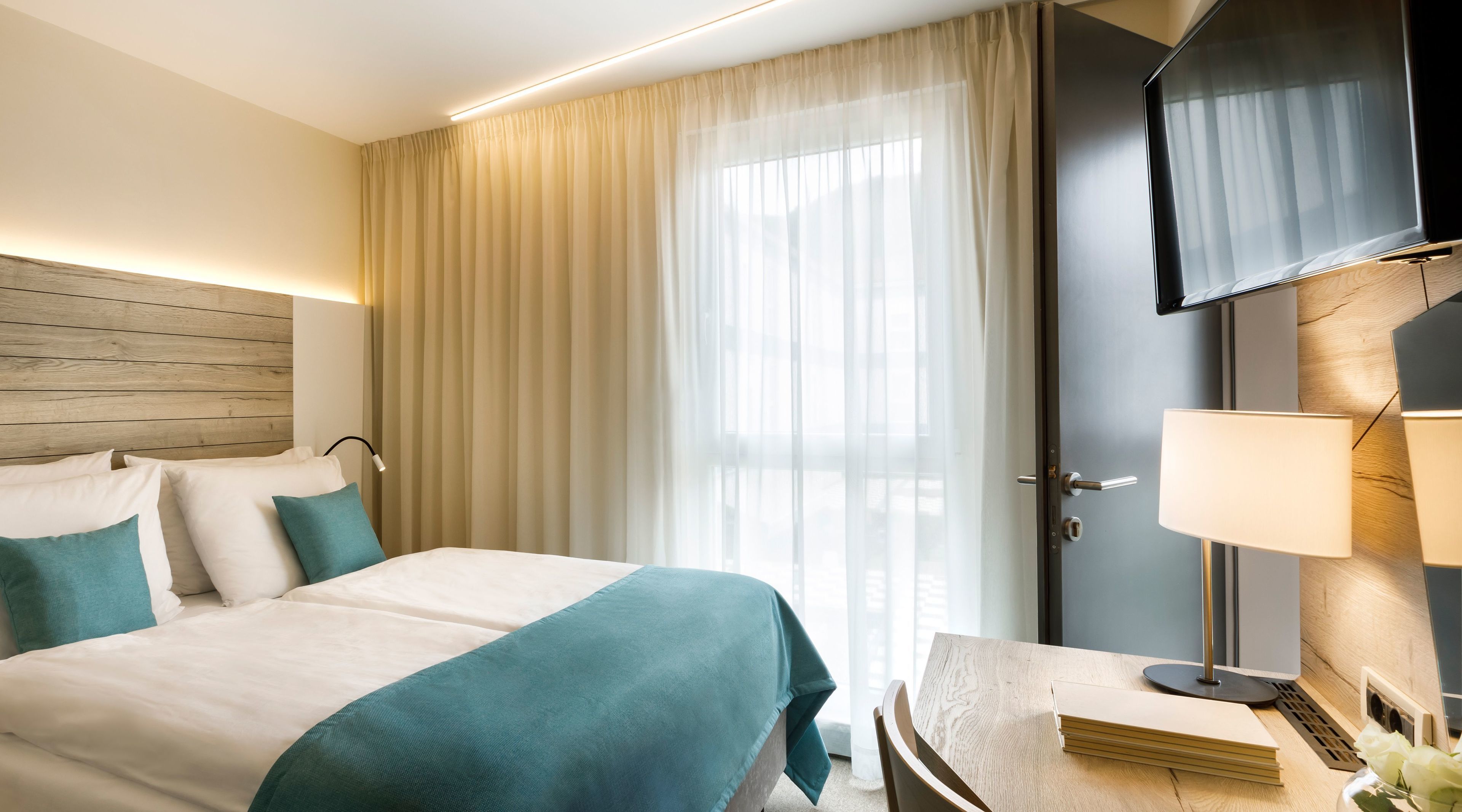 A hotel room with a bed, a desk, a TV, and a window with curtains.