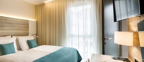 A hotel room with a bed, a desk, a TV, and a window with curtains.