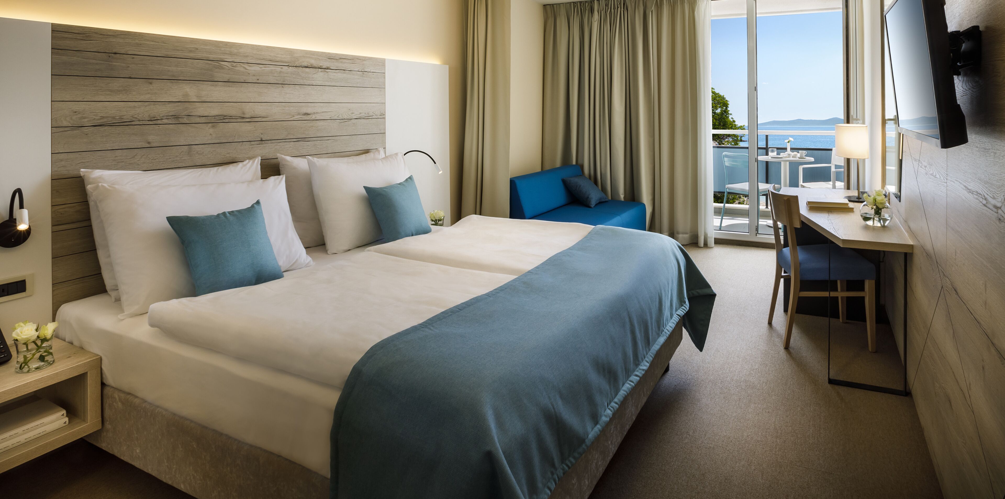 A hotel room with a large bed, a desk with a chair, a TV, and a balcony with a view.