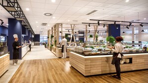Un interior de restaurante moderno con suelo de madera, una zona de buffet central y una escalera.