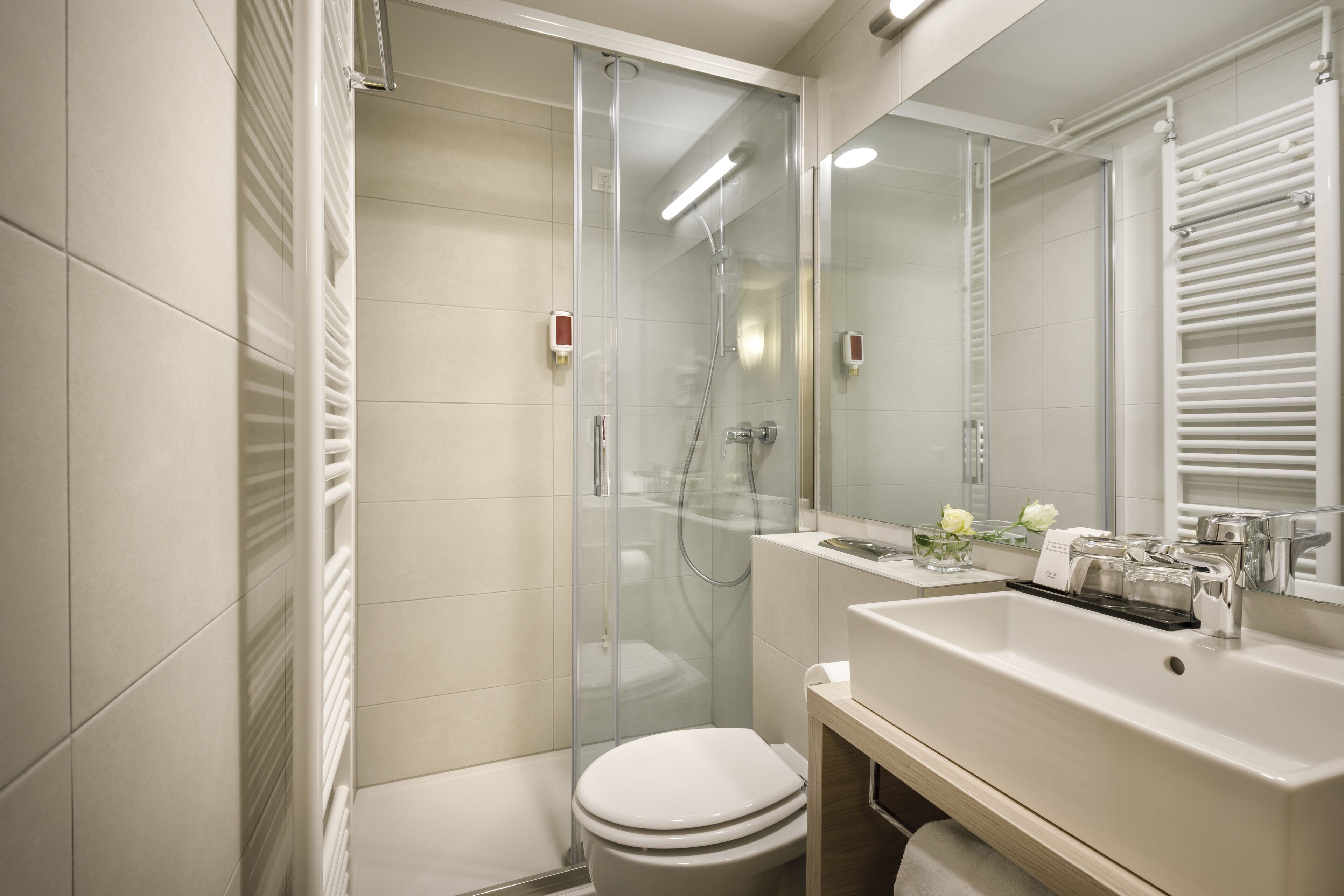 Un bany modern amb dutxa envidriada, vàter blanc i un lavabo amb mirall a sobre.