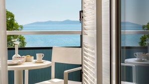 Un balcón con una mesa para dos, un florero con flores y vistas al mar y a las montañas.