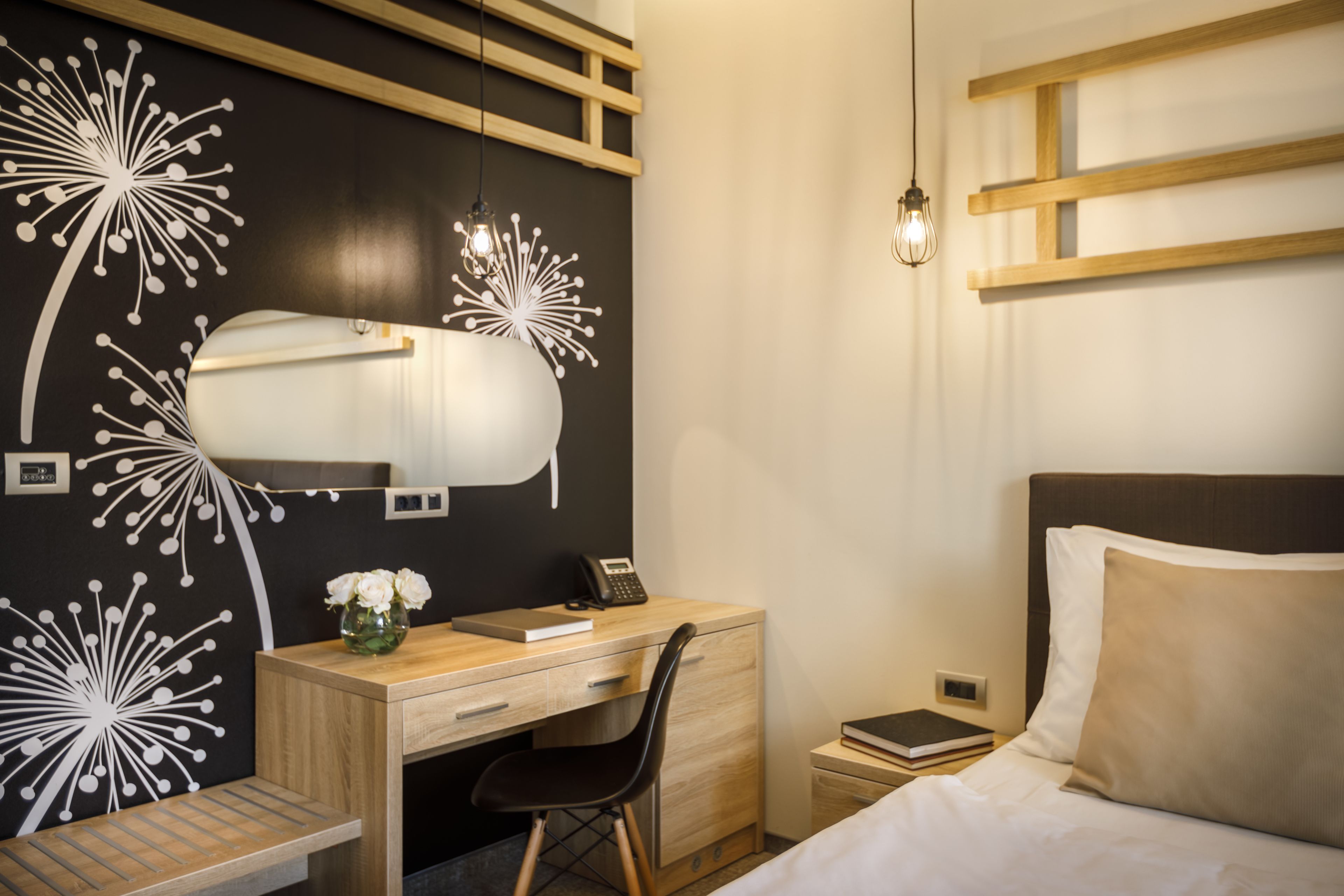 Una habitación de hotel moderna con un escritorio de madera, una silla, una cama con ropa blanca y una pared con un diseño floral blanco y negro original.