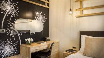 Una habitación de hotel moderna con un escritorio de madera, una silla, una cama con ropa blanca y una pared con un diseño floral blanco y negro original.