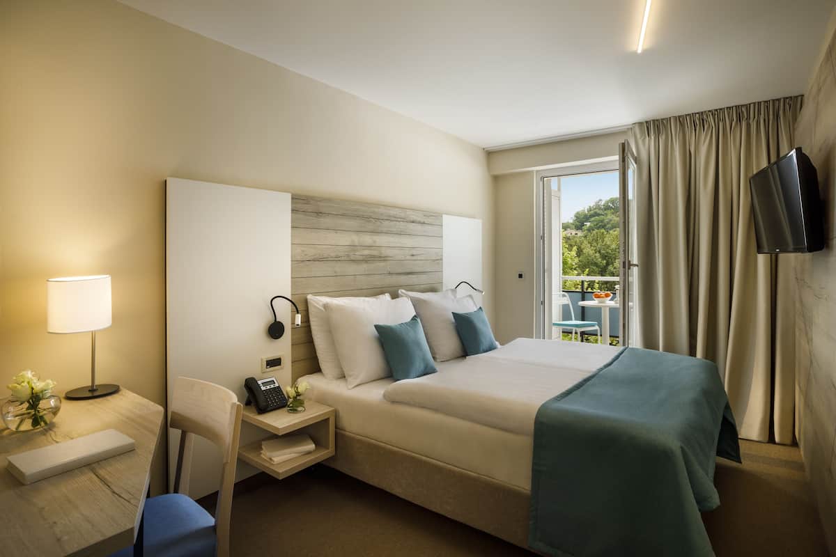 A hotel room with a bed, bedside table, lamp, chair, and a television on the wall.