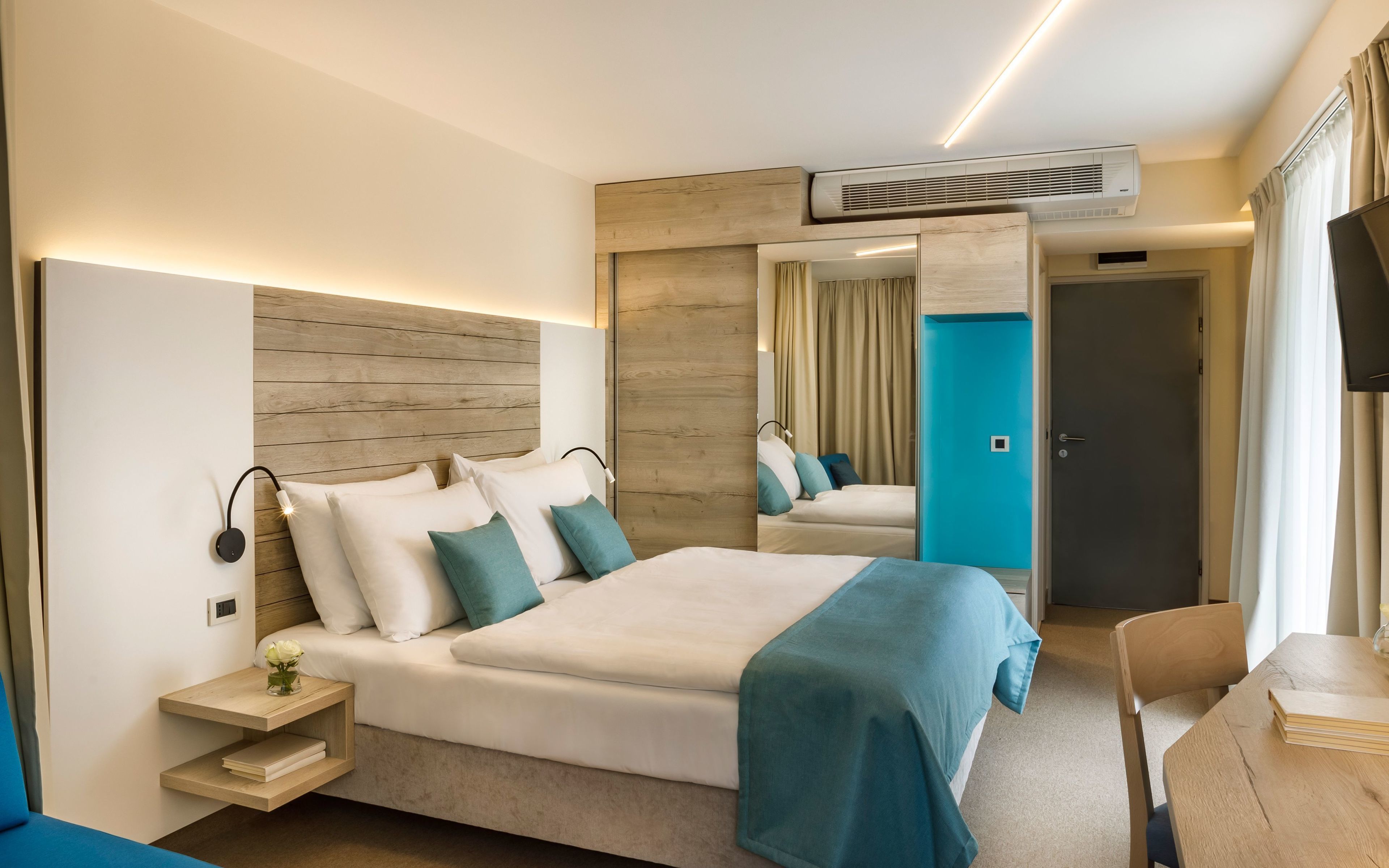 Quarto de hotel moderno com uma cama grande, mesas de cabeceira, uma escrivaninha e uma televisão.