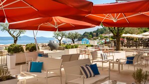 An outdoor seating area with white furniture and red umbrellas, overlooking a scenic coastal view.