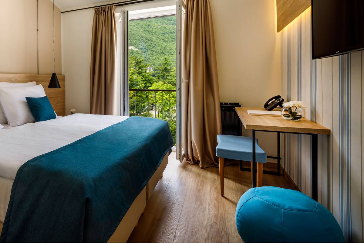 Een hotelkamer met een bed, een bureau, een stoel, een televisie en uitzicht op groen.