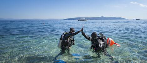 Two divers in clear water with a boat and distant land in the background.