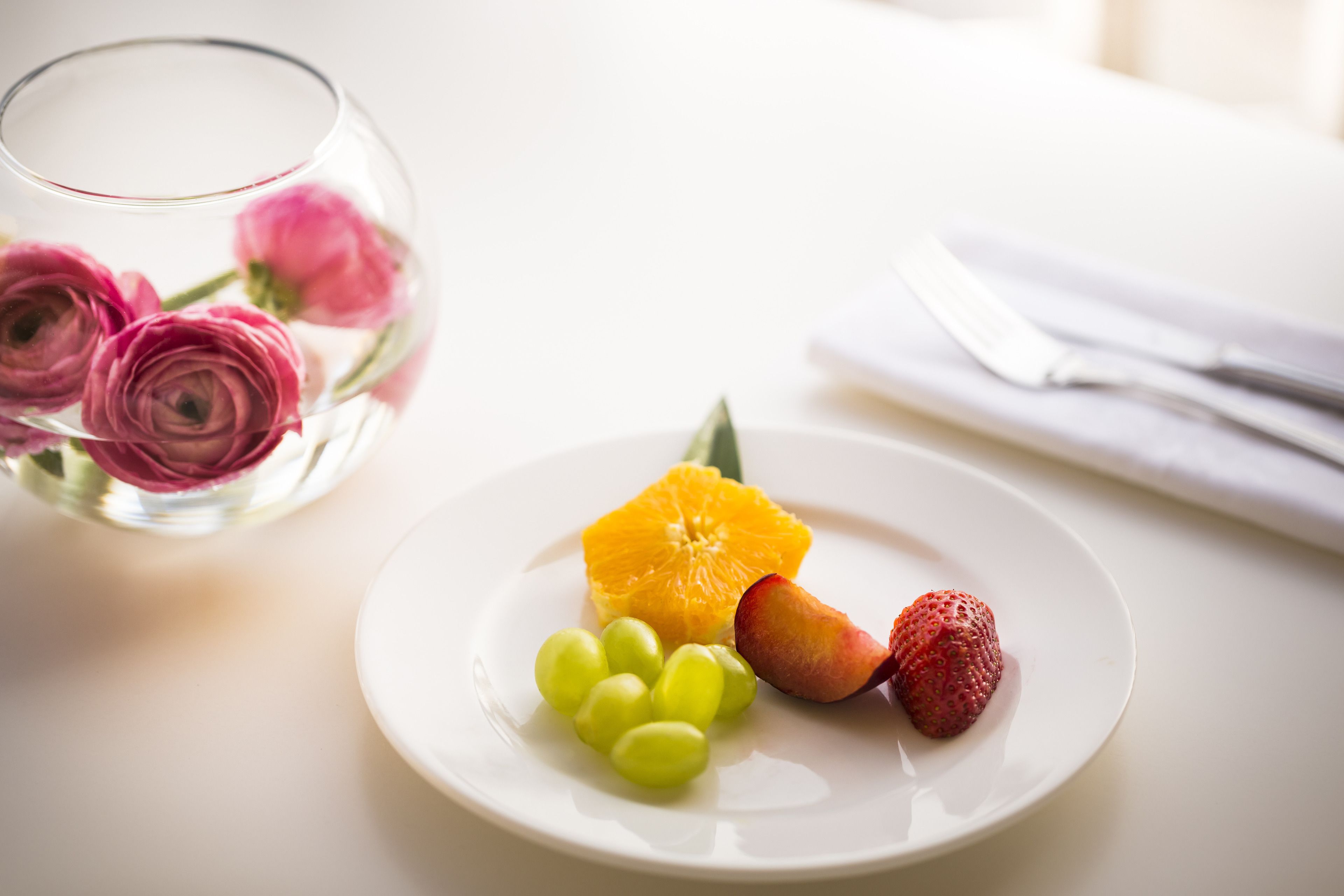 A white plate with grapes, an orange slice, and a strawberry on a table.
