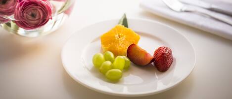 Un plato blanco con uvas, una rodaja de naranja y una fresa sobre una mesa.