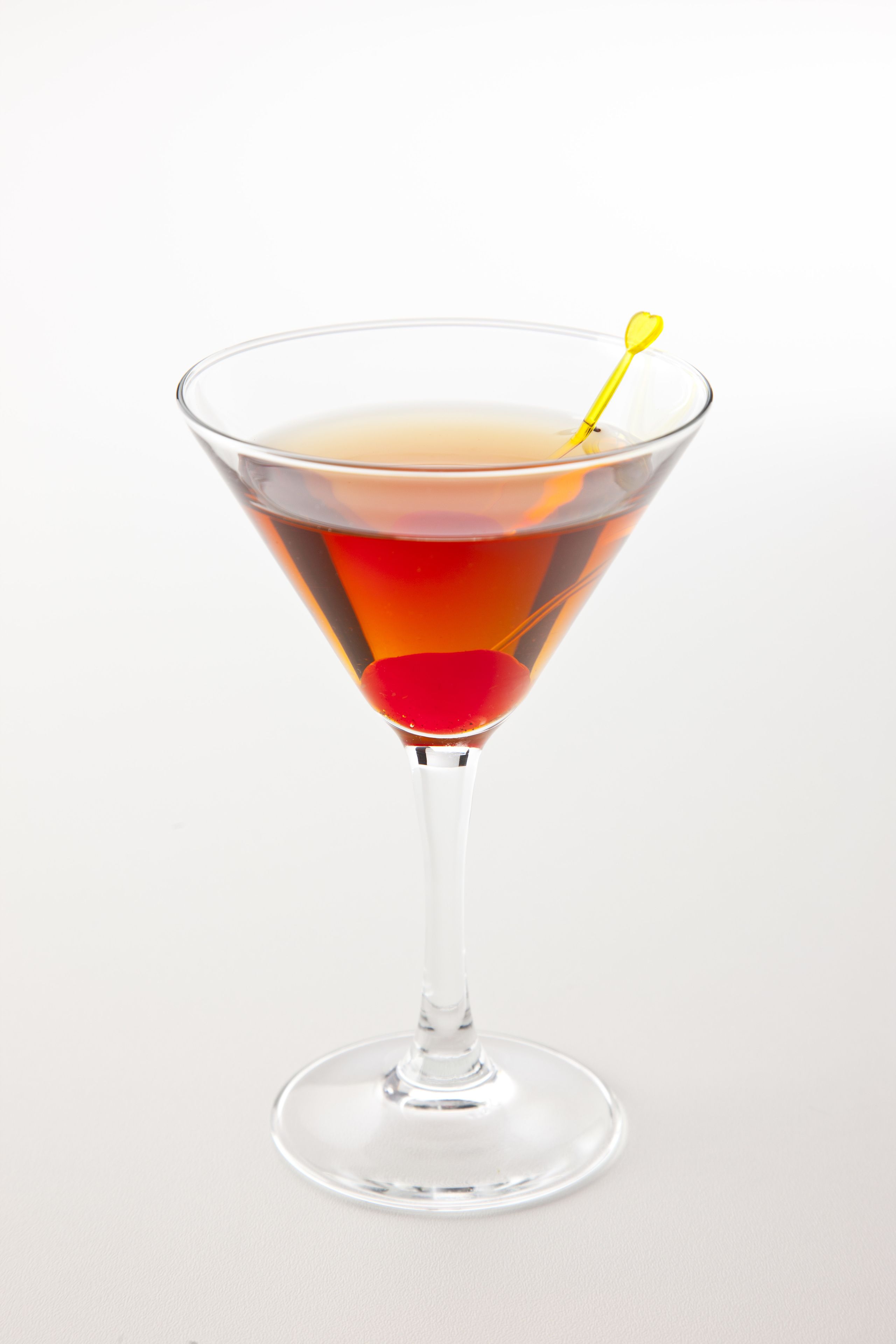Una copa de martini con una bebida en capas y un removedor con forma de corazón amarillo.