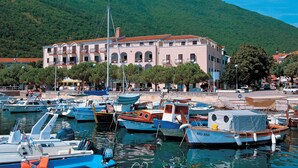 A marina with various boats docked, a building with balconies, and a hillside in the background.