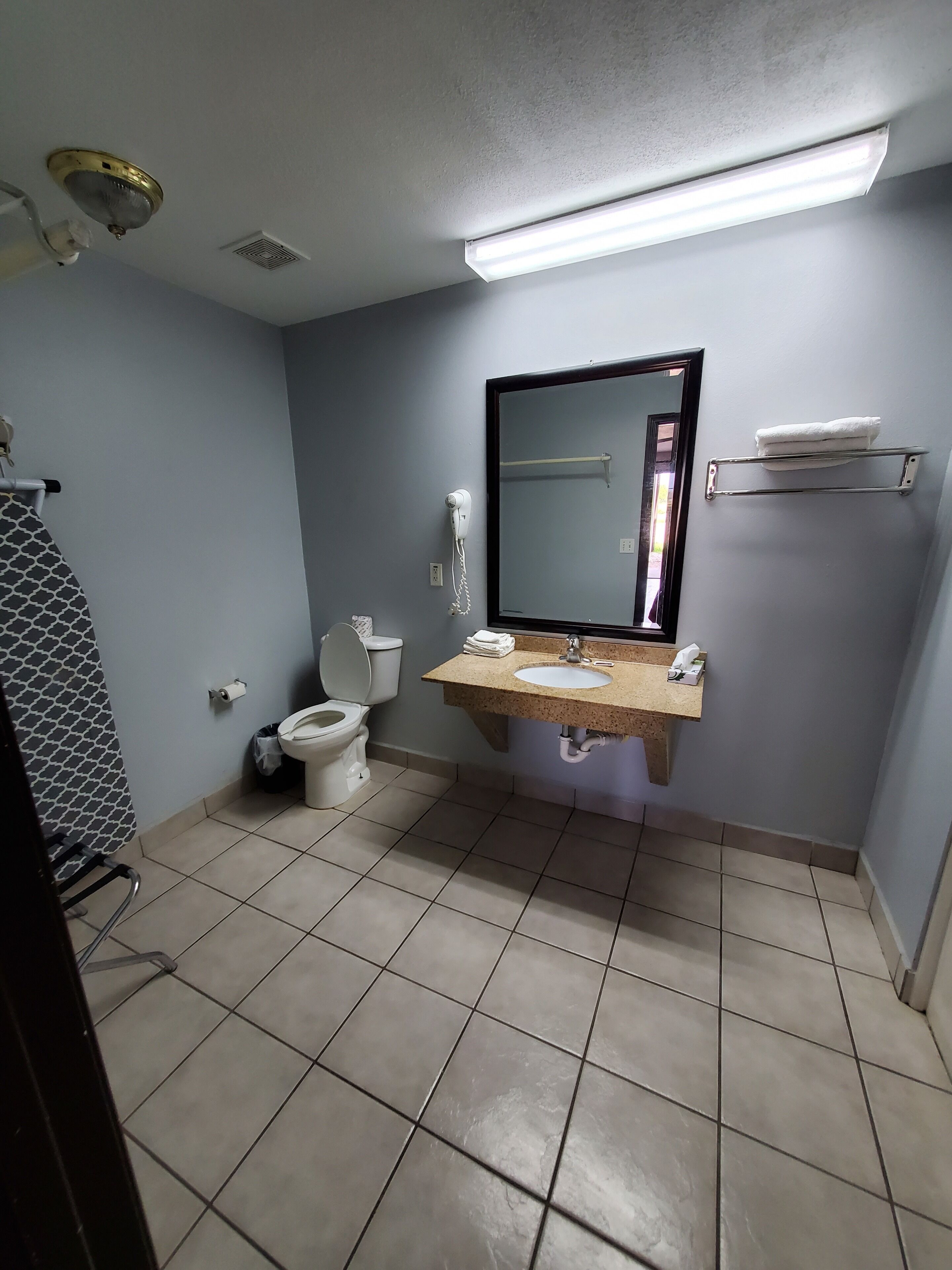 A bathroom with a toilet, sink, mirror, and towel rack.