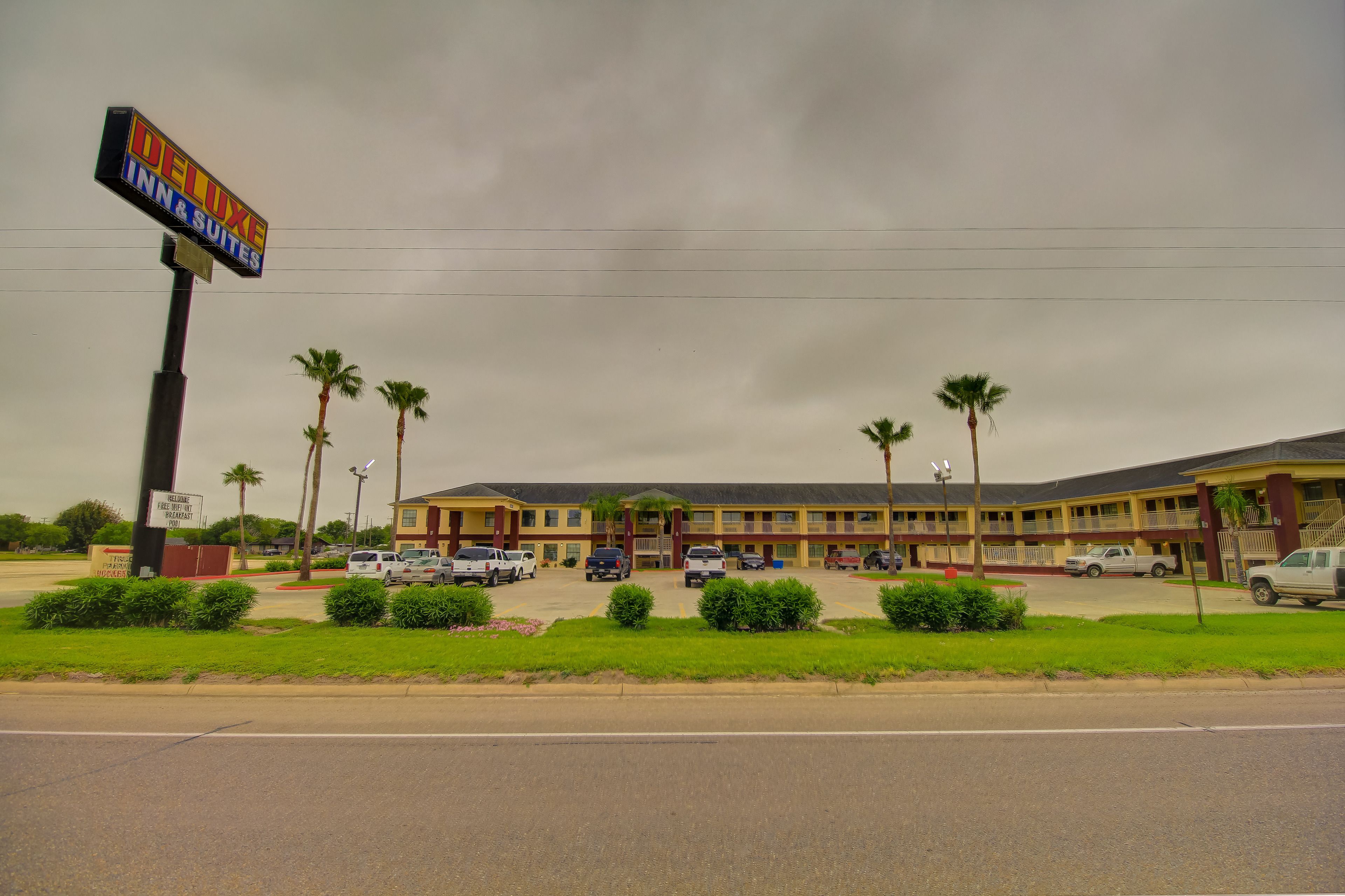 A hotel with a sign reading "Deluxe Inn Suites" and a parking lot with several cars.