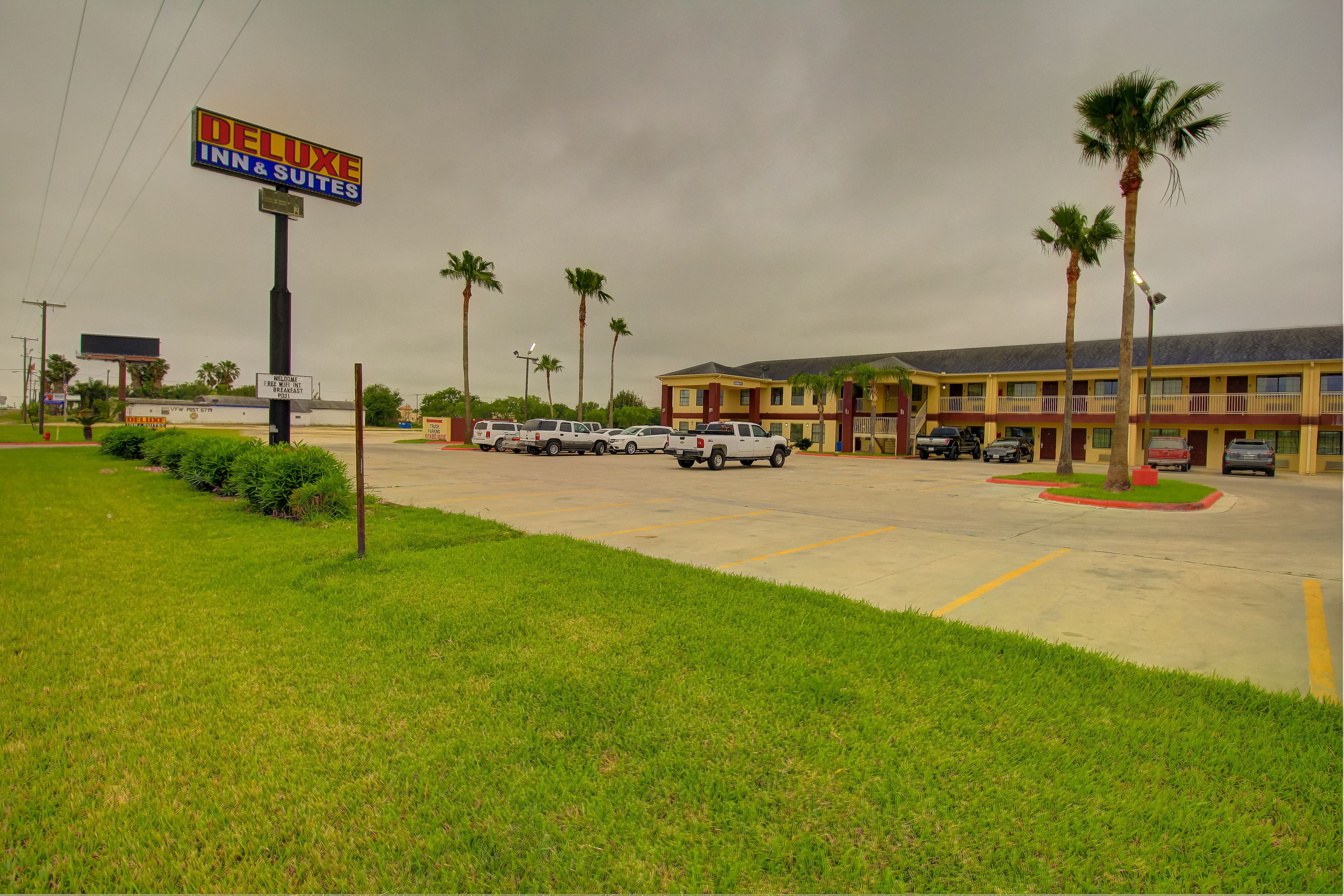 A hotel with a sign reading "Deluxe Inn & Suites" and a parking lot with several cars.