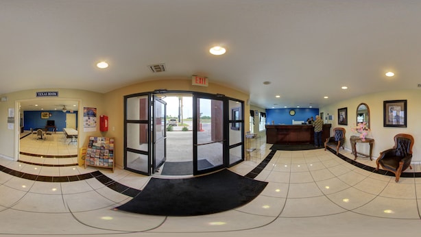 A lobby with a reception desk, a Texas room, and a waiting area with chairs and a small table. - Deluxe Inn & Suites (Raymondville)