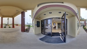 A hotel entrance with a curved glass door, a covered outdoor area, and a view of the parking lot. - Deluxe Inn & Suites (Raymondville)