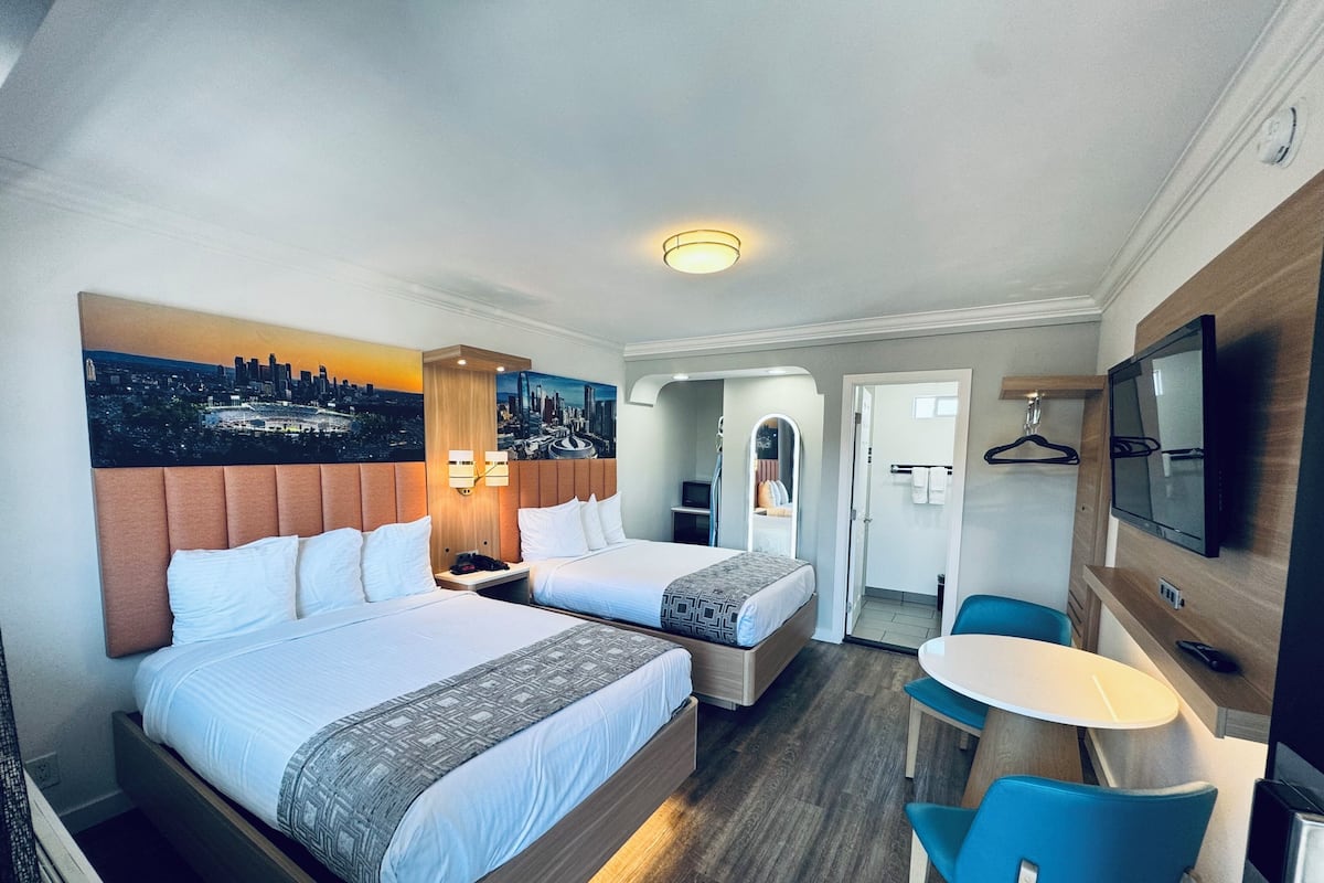 A hotel room with two beds, a TV, a desk, and a chair.