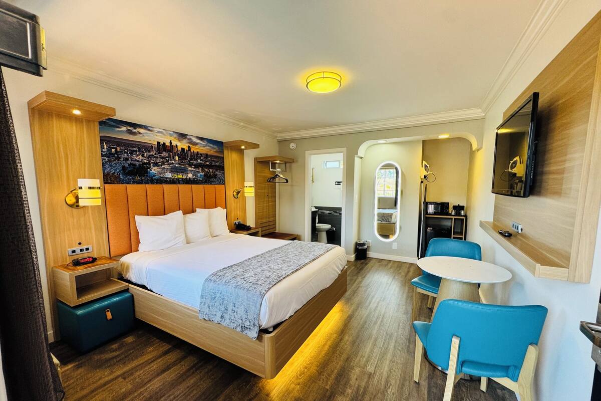 A hotel room with a bed, a desk, a chair, a TV, and a bathroom.