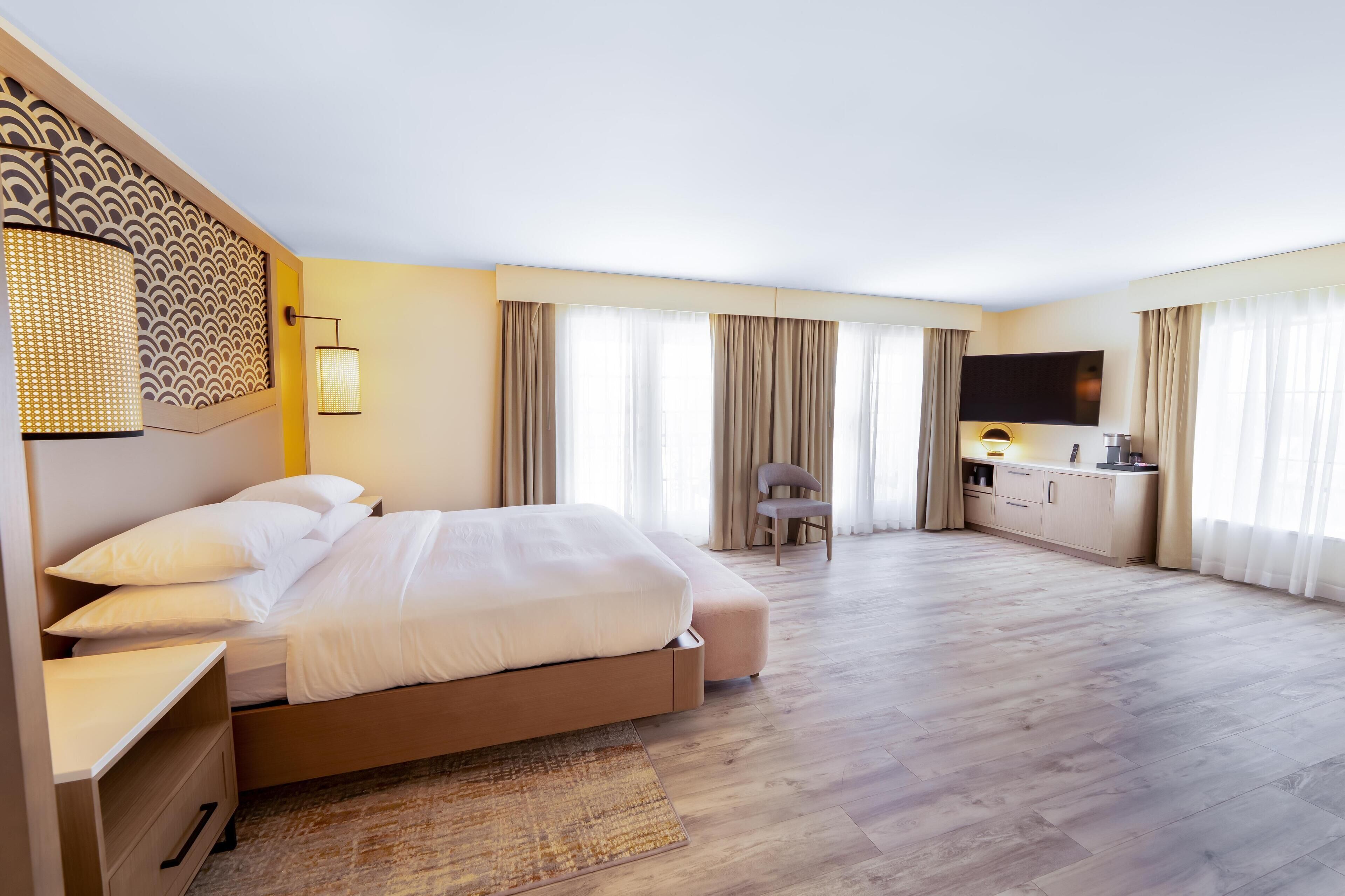 A modern hotel room with a large bed, a desk, a chair, and a TV.
