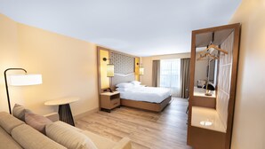A hotel room with a bed, a sofa, a bedside table, a lamp, and a mirror.