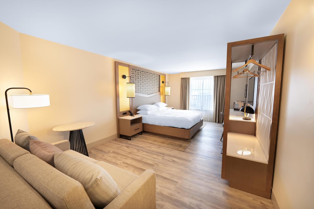 A hotel room with a bed, a sofa, a bedside table, a lamp, and a mirror.