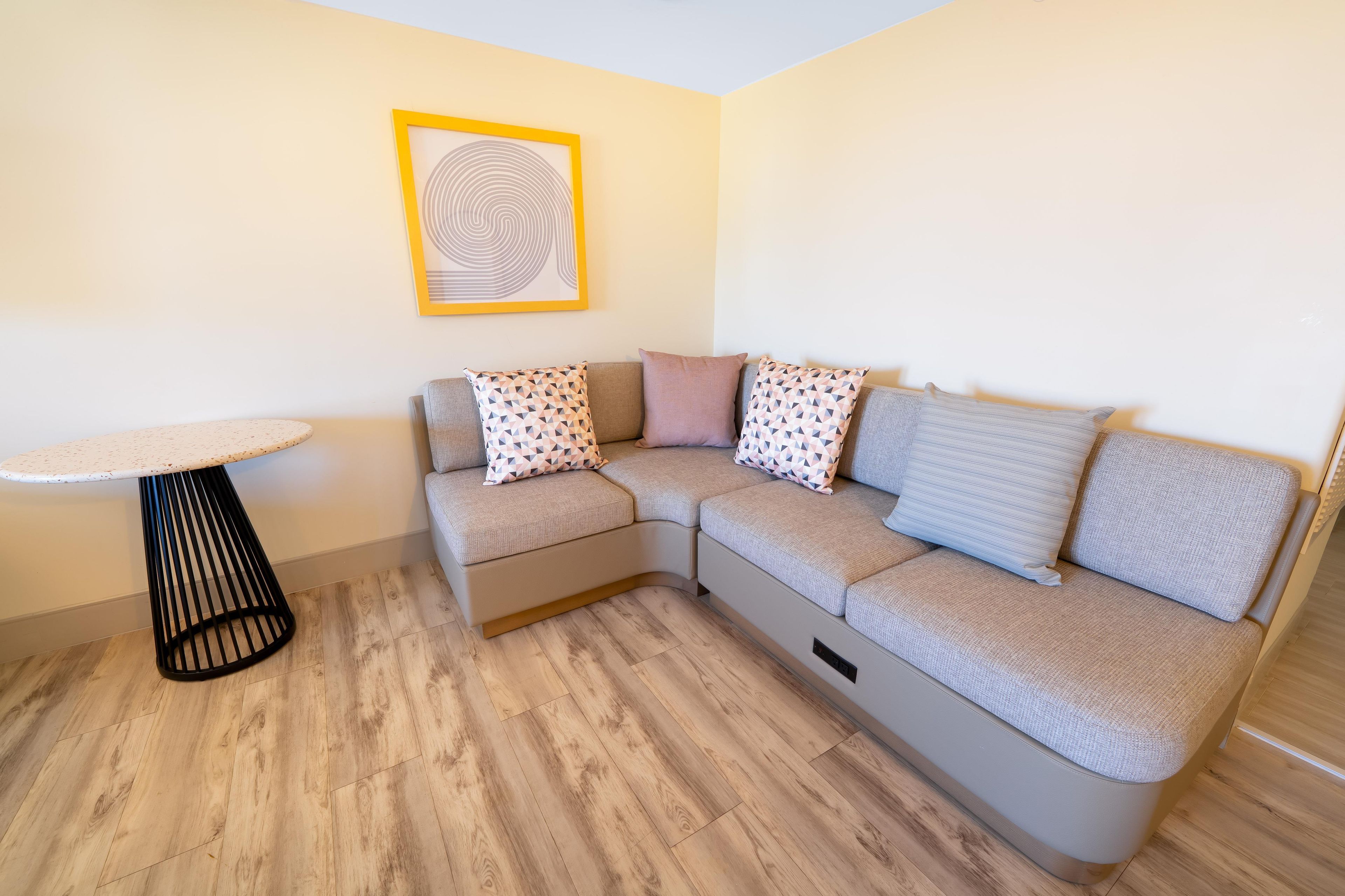 A modern living room with a sectional sofa, a small round table, and a patterned wall art piece.