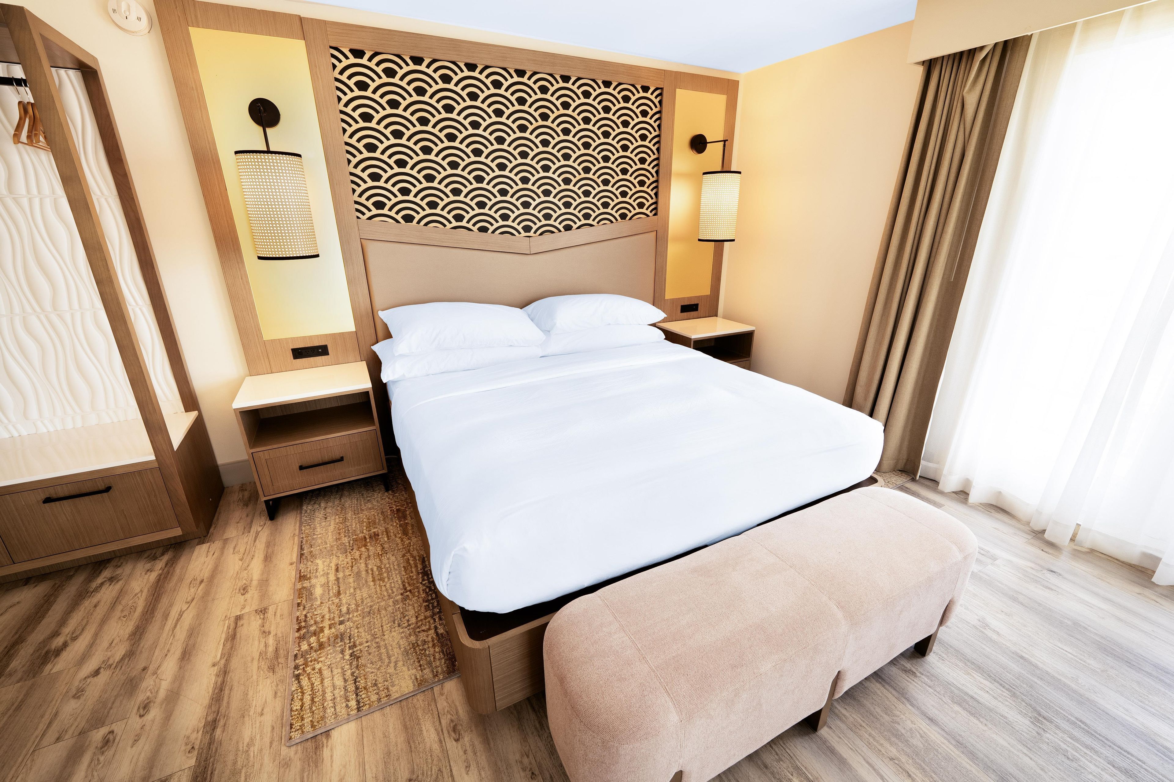 Ett hotellrum med en stor säng, sängbord, en garderob och en dekorativ sänggavel.