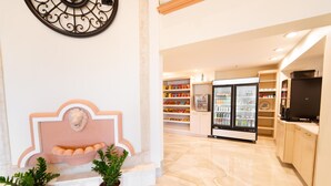 A modern hotel lobby with a marble floor, a decorative wall piece, a refrigerator, and potted plants.