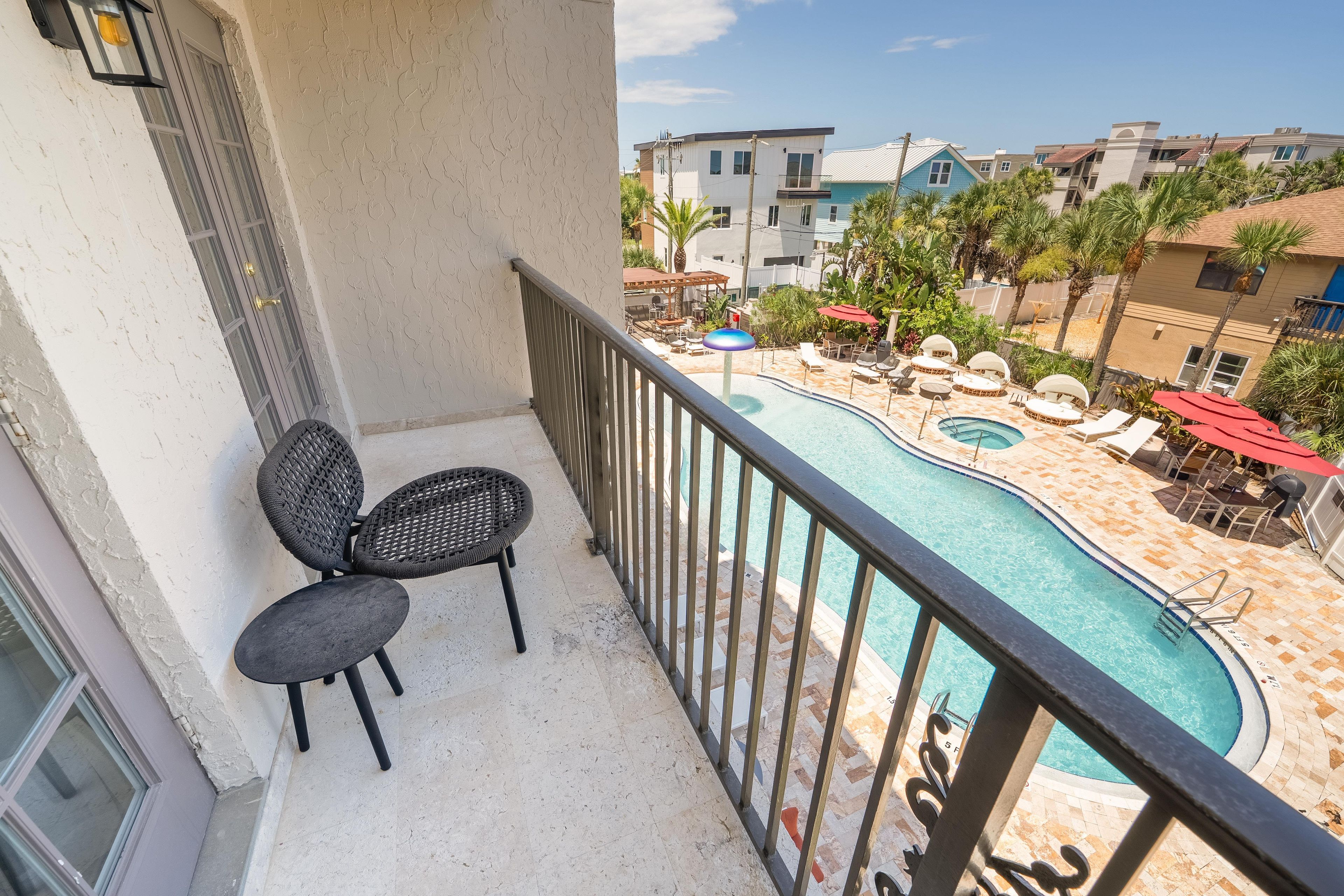 A balcony with a view of a swimming pool and lounge chairs.