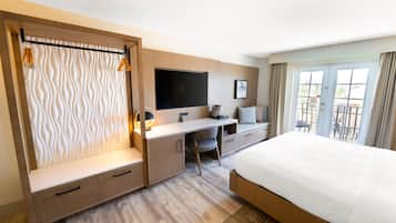 A hotel room with a bed, a desk, a TV, and a balcony with a view.