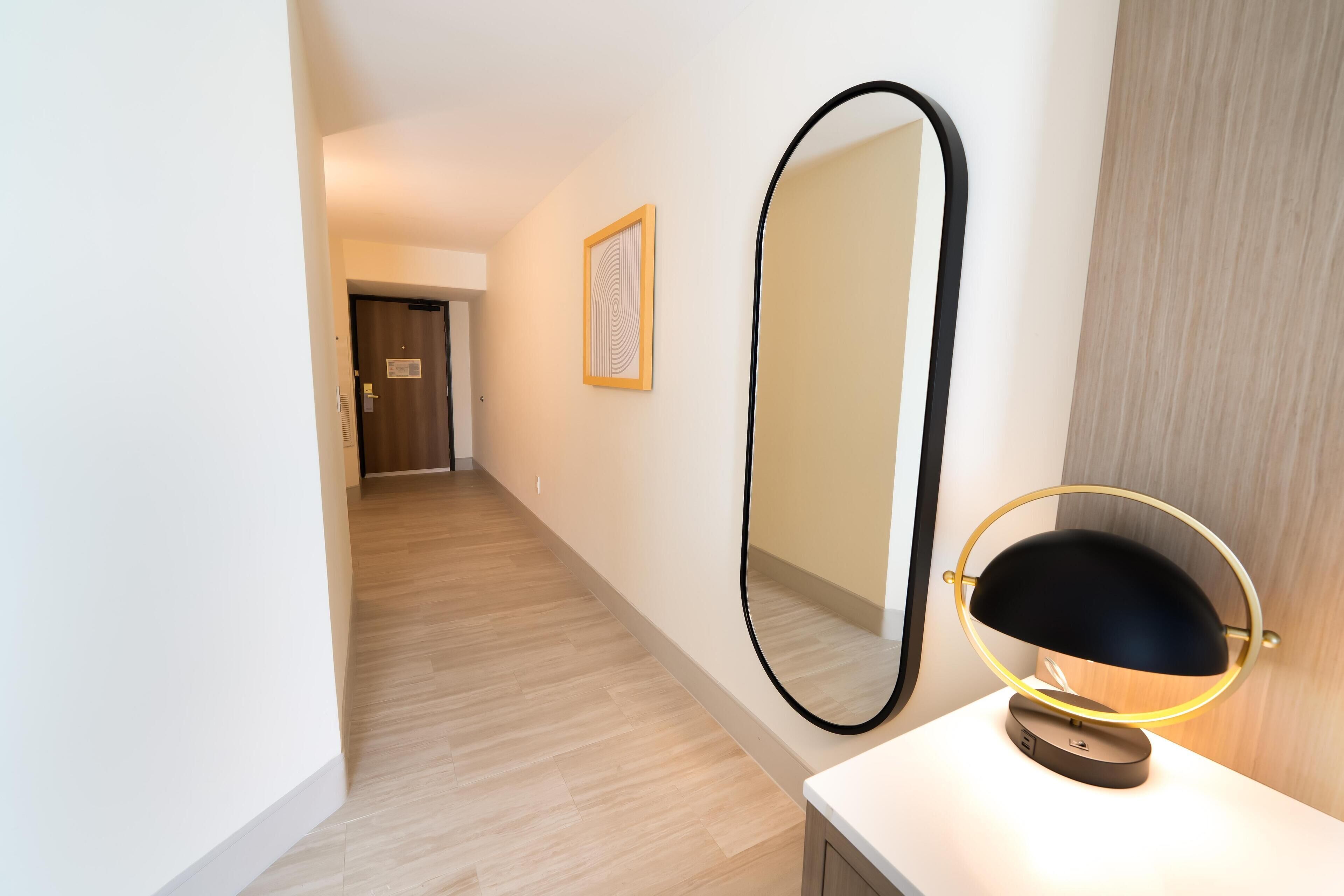 A hallway with a large mirror and a desk lamp.