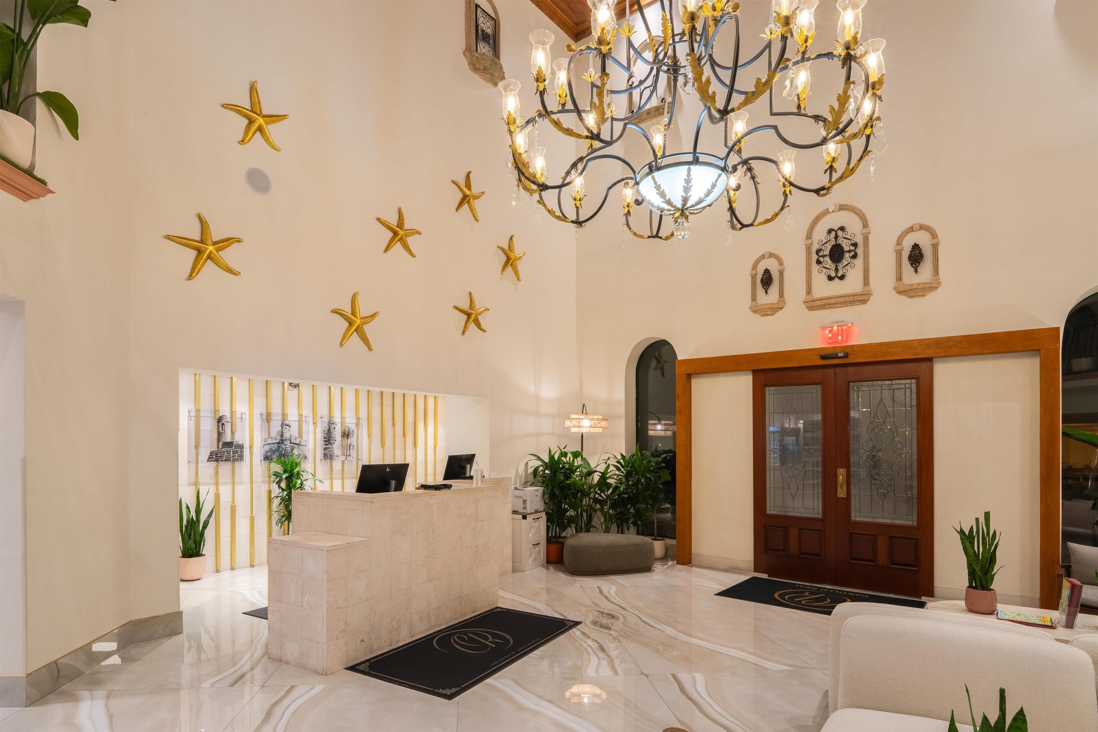A hotel lobby with a reception desk, a chandelier, star decorations, and a wooden door.
