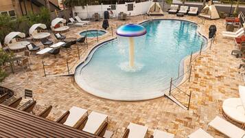 Un área de piscina con sillones reclinables, un jacuzzi y una pequeña cascada.