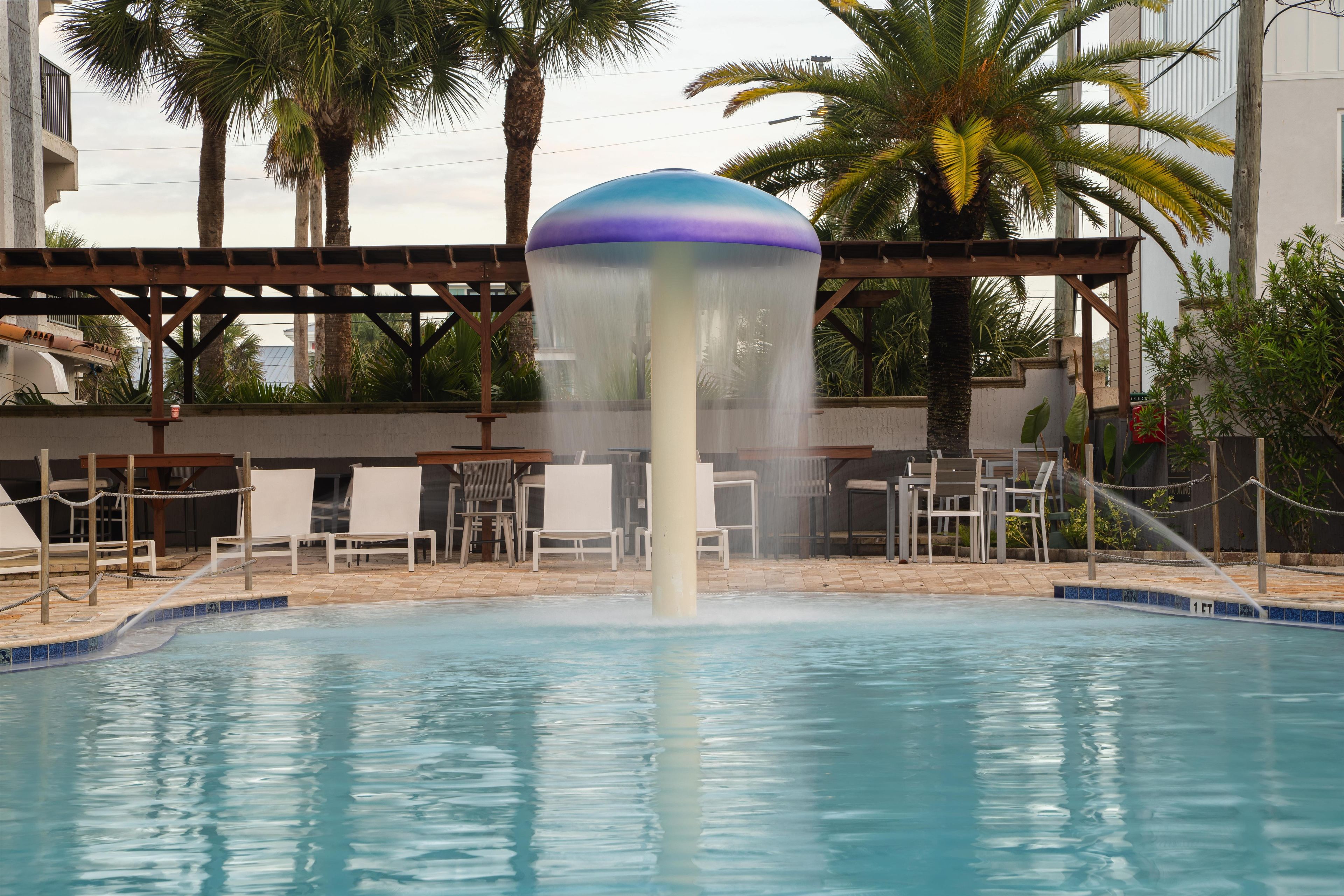 A pool with a water feature, surrounded by lounge chairs and palm trees.