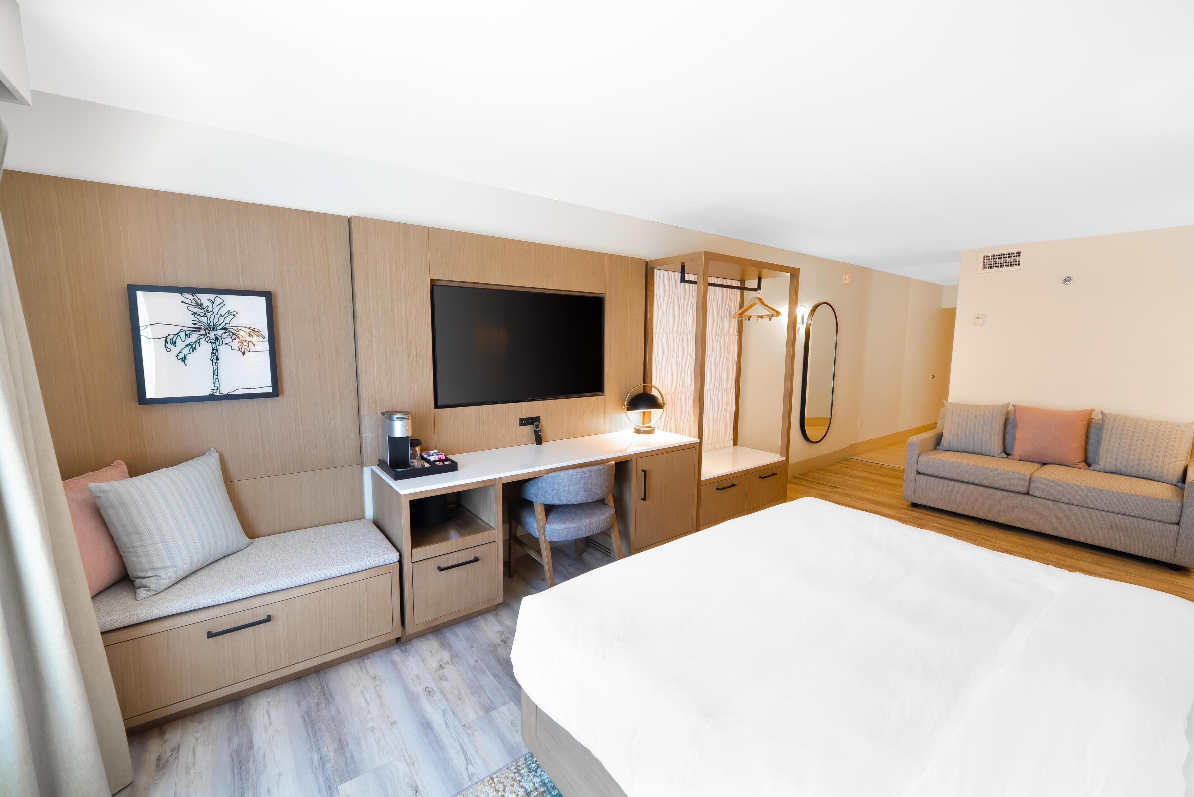 Una habitación de hotel moderna con cama, escritorio con silla, sofá, televisor y un cuadro en la pared.