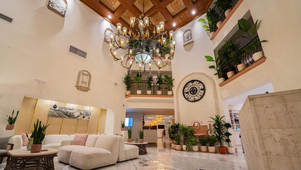 A spacious lobby with a chandelier, sofas, potted plants, and a large wall clock. - Castillo Real St. Augustine Beach,Tapestry Collection Hilton (St. Augustine)