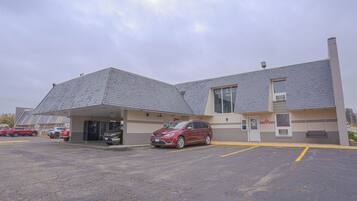A building with a parking lot, a covered parking area, and a red car parked in front.