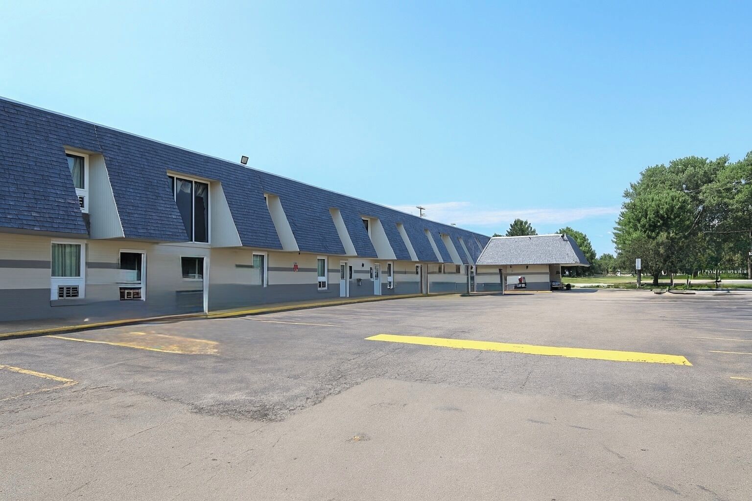 A row of motel rooms with a parking lot in front.