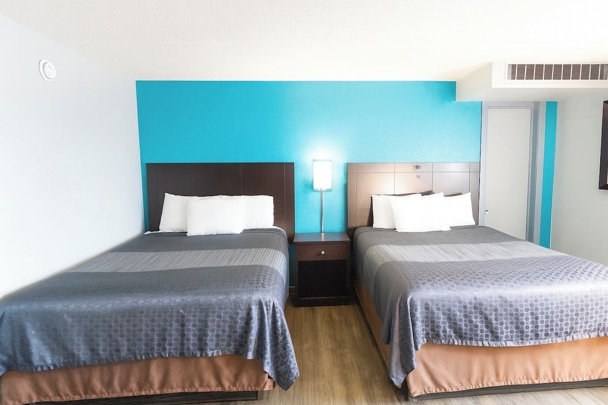 A hotel room with two beds, each with a headboard, a nightstand, and a wall-mounted lamp.